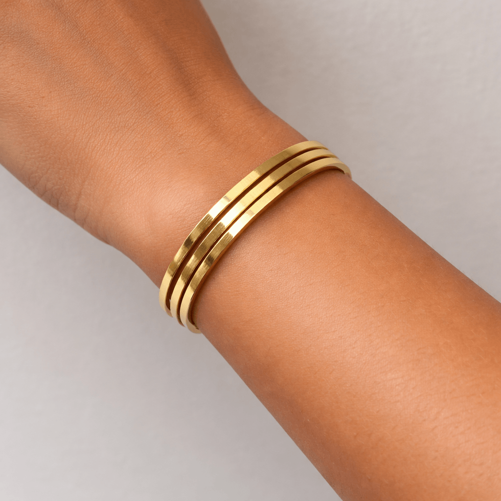Gold bracelet on a person's wrist against a neutral background