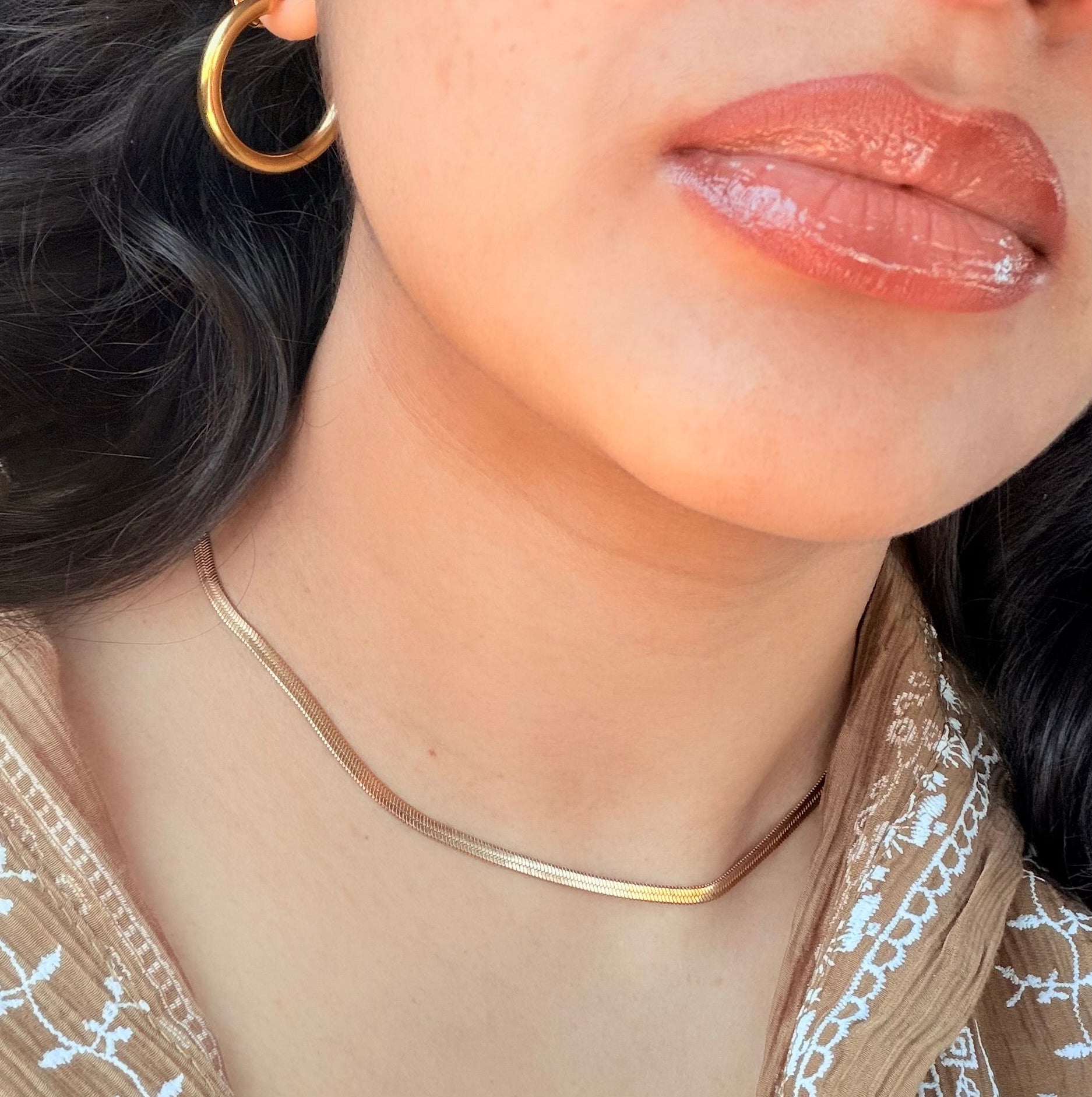 Close-up of a person wearing a gold necklace and hoop earring.