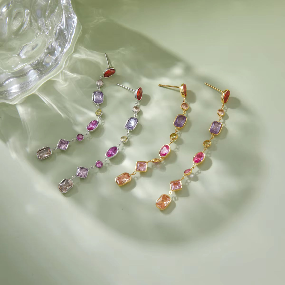 Colorful gemstone earrings on a light green surface
