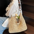 Person holding a woven handbag with wooden handle and beads, sitting on a wooden bench.