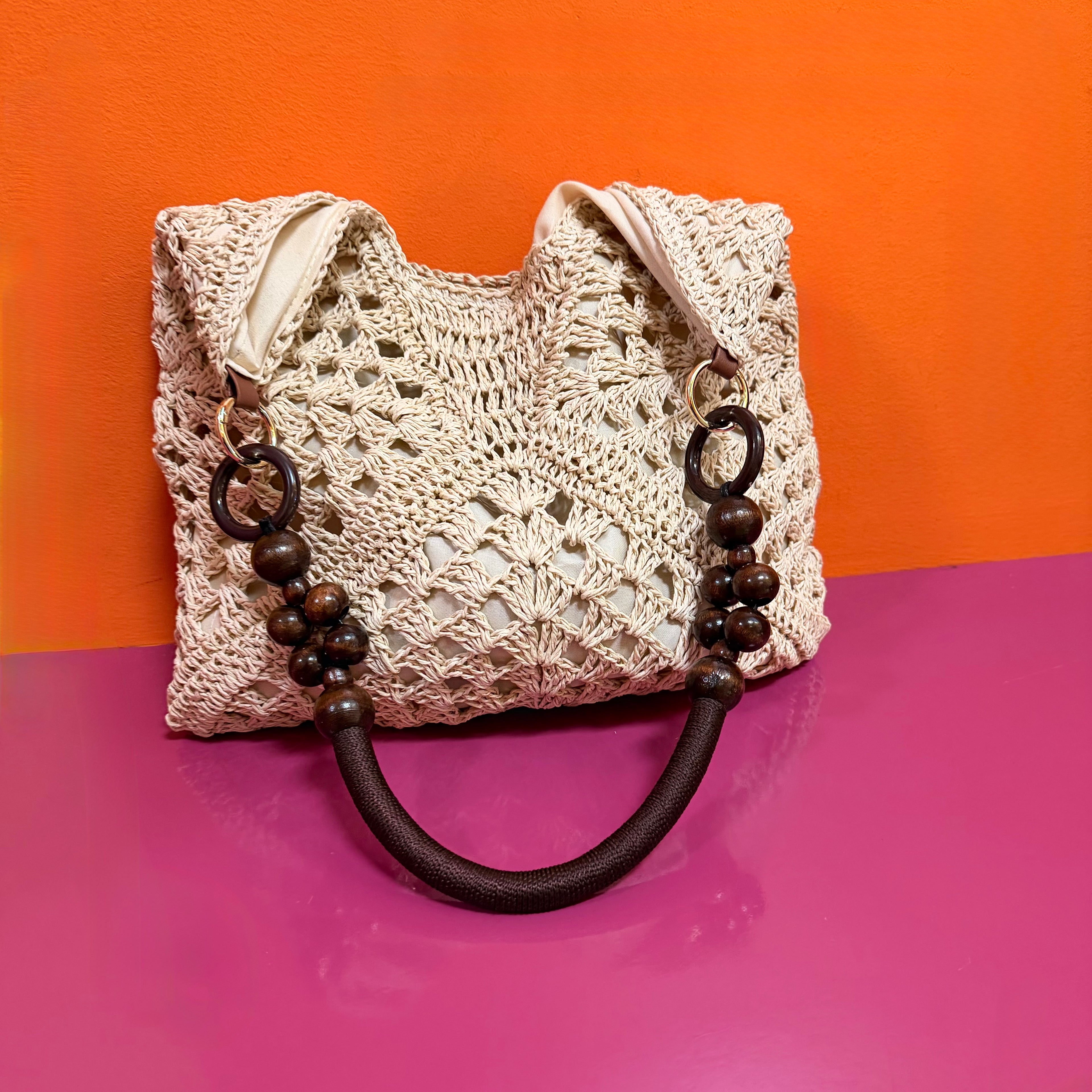 Crocheted handbag with wooden beads on a pink and orange background